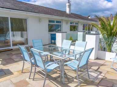An outdoor patio with a glass table and six blue chairs at 3 Madoc View in Bwlchtocyn near Abersoch