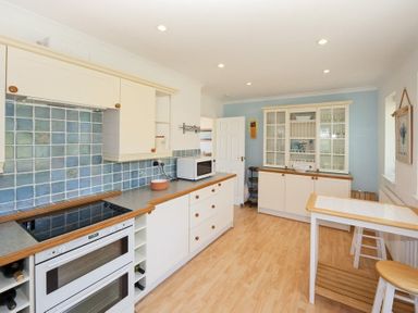 A kitchen with white cabinets blue tiled backsplash and a small table with stools at 3 Madoc View Bwlchtocyn near Abersoch
