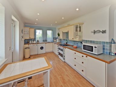 A kitchen with white cabinets blue tiled backsplash wooden countertop and appliances at 3 Madoc View in Bwlchtocyn near Abersoch