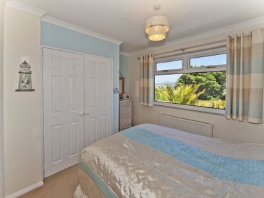 A bedroom with a bed a window curtains a chest of drawers and a double wardrobe at 3 Madoc View in Bwlchtocyn near Abersoch