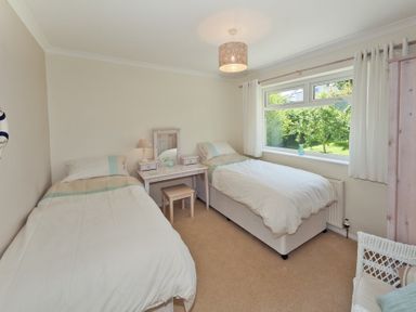 A bedroom with two single beds a desk with a mirror and lamp and a window showing garden view at 3 Madoc View Bwlchtocyn near Abersoch