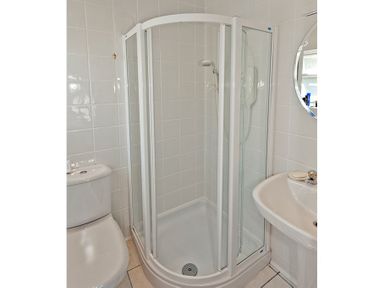 A bathroom with a corner shower enclosure a toilet and a sink with a round mirror at 3 Madoc View Bwlchtocyn near Abersoch
