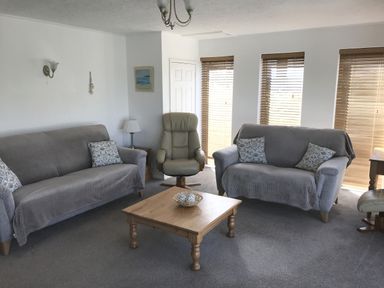 A living room with two sofas, an armchair, wooden coffee table, lamp, and windows with wooden blinds at 3 Madoc View in Bwlchtocyn near Abersoch