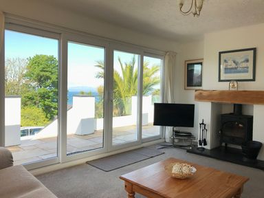 A living room with large glass sliding doors overlooking a balcony with trees and sea beyond at 3 Madoc View in Bwlchtocyn near Abersoch