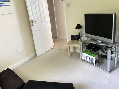 A living room with a television on a glass stand next to a small table with a lamp and a device at 3 Madoc View Bwlchtocyn near Abersoch