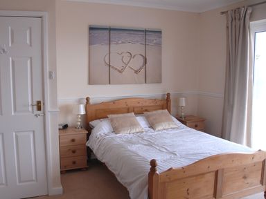 A bedroom with a wooden double bed, two bedside tables with lamps, and a three-panel wall art above the bed at 3 Madoc View in Bwlchtocyn near Abersoch