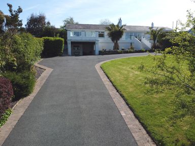 A driveway leading to a white house with a garage and stairs surrounded by green lawn and bushes at 3 Madoc View in Bwlchtocyn near Abersoch