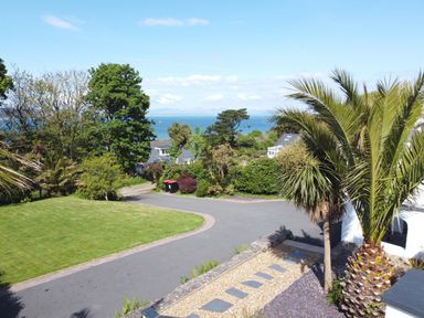 A garden with a palm tree lawn and driveway overlooking the sea at 3 Madoc View in Bwlchtocyn near Abersoch
