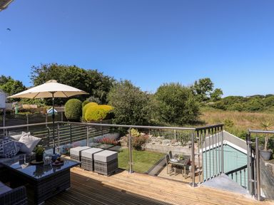 An outdoor deck with seating and an umbrella overlooking a garden and green landscape at The Anchorage in Abersoch