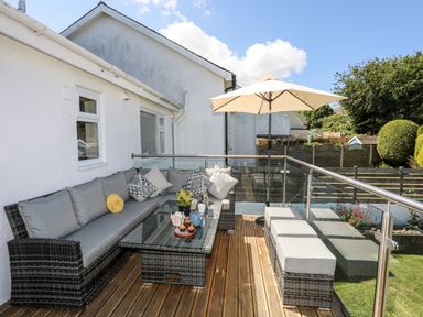 An outdoor patio with wicker furniture and cushions a table with food and umbrella over seating at The Anchorage in Abersoch