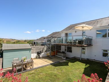 A backyard with a patio table and chairs near a shed and a balcony with outdoor furniture and umbrella at The Anchorage in Abersoch
