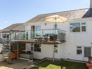A balcony with glass railing and umbrella with spiral staircase leading to a patio below at The Anchorage in Abersoch