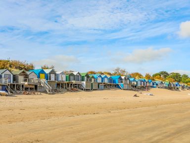 A row of beach huts on stilts along a sandy beach with blue sky at The Anchorage in Abersoch