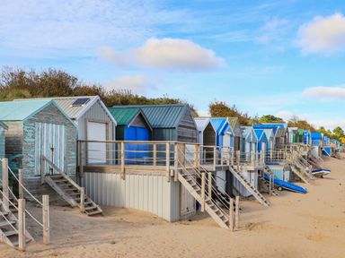 A row of colorful beach huts on sandy ground with wooden stairs leading to each hut at The Anchorage in Abersoch