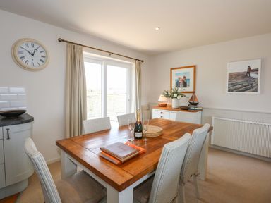 A dining room with a wooden table and six chairs near sliding glass doors at The Anchorage in Abersoch