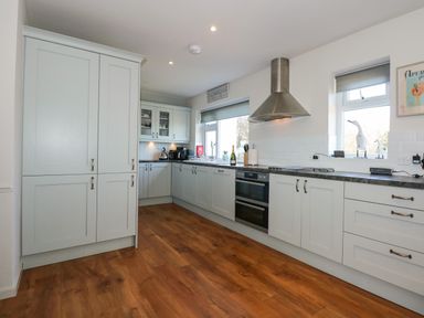 A kitchen with white cabinets a stainless steel oven and hood and wooden floor at The Anchorage in Abersoch