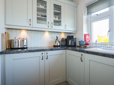 A kitchen corner with cabinets countertop toaster kettle coffee machine and window at The Anchorage in Abersoch