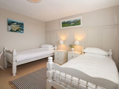 A bedroom with two single beds bedside tables lamps and paintings at The Anchorage in Abersoch