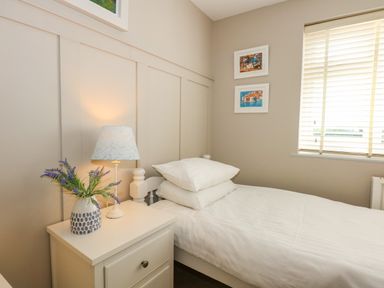 A bedroom with a single bed next to a nightstand with a lamp and vase of flowers at The Anchorage in Abersoch