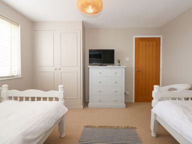 A bedroom with two single beds a white dresser with a television on top a wooden door and a built in wardrobe at The Anchorage in Abersoch