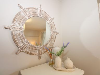 A decorative mirror with a wooden frame above a white table with vases and artificial flowers at The Anchorage in Abersoch