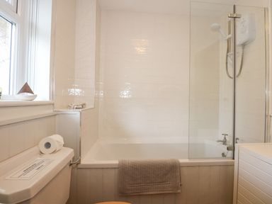 A bathroom with a bathtub shower combination a toilet with a roll of toilet paper and a towel hanging on the bathtub at The Anchorage in Abersoch