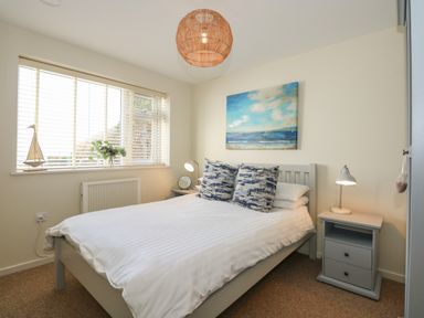 A bedroom with a double bed white blinds bedside tables and a painting above the bed at The Anchorage in Abersoch