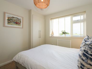 A bedroom with a bed and pillows a window with blinds a built in wardrobe and framed artwork at The Anchorage in Abersoch