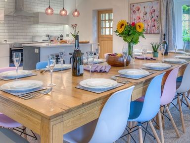 A dining table set with plates cutlery and glasses with colorful chairs in a kitchen at The Coach House in Abersoch