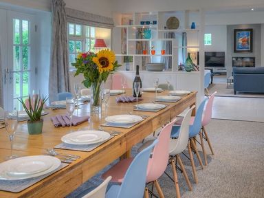 A dining room with a wooden table set with plates glasses cutlery and flowers surrounded by colorful chairs at The Coach House in Abersoch