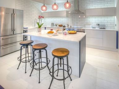 A modern kitchen with a central island with three stools a refrigerator oven and white tiled walls at The Coach House in Abersoch