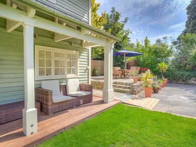 A porch with a wicker sofa and cushions and a patio area with a table umbrella and chairs at The Coach House in Abersoch