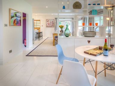 A dining area with a round table and two chairs and an open shelving unit separating it from another dining table at The Coach House in Abersoch