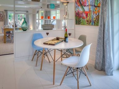A dining area with a round white table and three chairs with a colorful painting and a lamp nearby at The Coach House in Abersoch