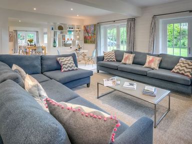 A living room with two blue sofas a glass coffee table and books at The Coach House in Abersoch
