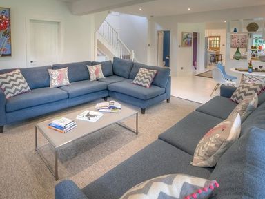 A living room with blue sofas, a coffee table with books, and a view into a dining area at The Coach House in Abersoch