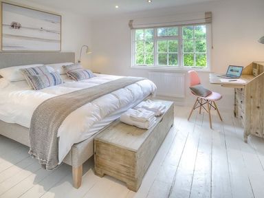 A bedroom with a double bed a wooden chest folded towels a desk with a laptop and a pink chair under a window at The Coach House in Abersoch