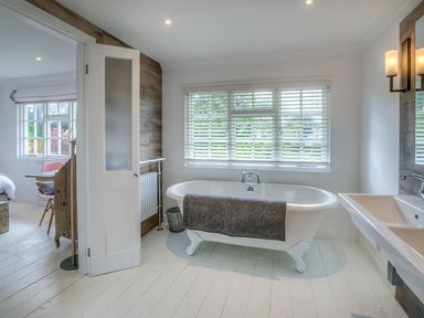 A bathroom with a freestanding clawfoot bathtub a towel a window with blinds and a double sink next to a bedroom at The Coach House in Abersoch