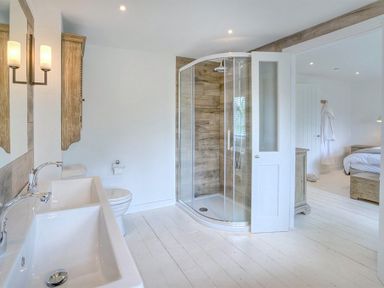 A bathroom with a double sink vanity toilet and glass shower next to a bedroom at The Coach House in Abersoch