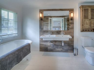 A bathroom with a freestanding bathtub towel double sink mirror toilet and wooden cabinet at The Coach House in Abersoch