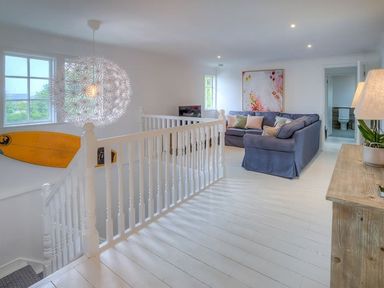 An upstairs sitting area with a blue sofa and pillows a wooden sideboard and a decorative light fixture at The Coach House in Abersoch