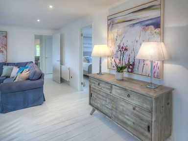 A room with a blue sofa and wooden sideboard with two lamps and a painting at The Coach House in Abersoch