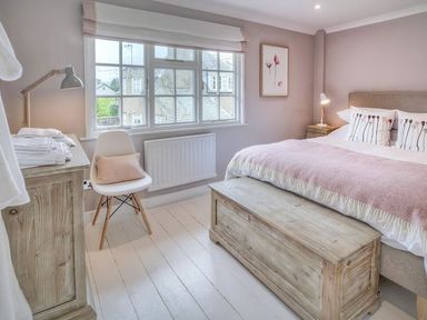 A bedroom with a bed a wooden chest a chair a lamp and a window at The Coach House in Abersoch