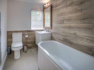 A bathroom with a bathtub toilet sink mirror and window at The Coach House in Abersoch