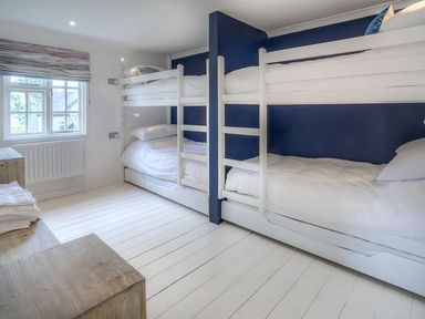 A bedroom with two sets of white bunk beds and a window with a wooden bench at The Coach House in Abersoch
