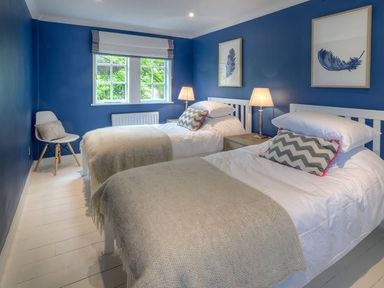 A bedroom with two single beds lamps a chair and windows at The Coach House in Abersoch
