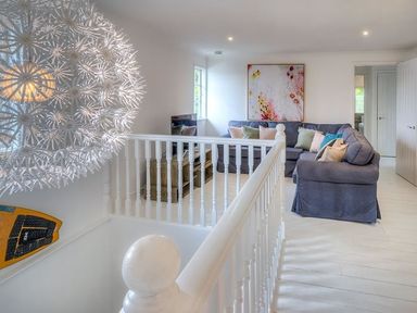 A sitting area with a grey sectional sofa and cushions a television and a large decorative light fixture at The Coach House in Abersoch