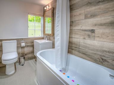A bathroom with a toilet sink and bathtub with wood panel walls at The Coach House in Abersoch