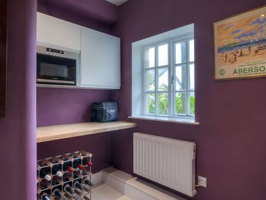 A small kitchen area with a wooden countertop wine rack microwave and a window at The Coach House in Abersoch