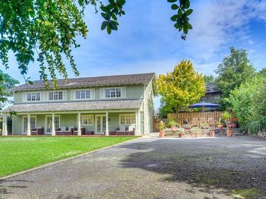 A two-story house with a covered porch and outdoor seating next to a patio with chairs and plants at The Coach House in Abersoch